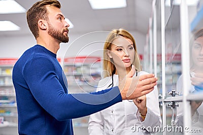 Young helpful female druggist dealing with a male customer, explaining a prescription Stock Photo