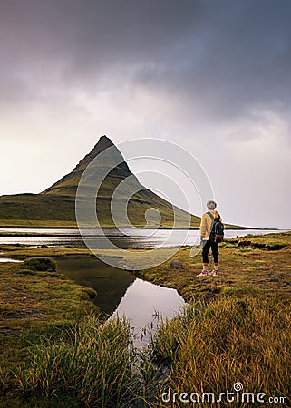 Young hiker with a backpack looks at the Kirkjufell mountain in Iceland Stock Photo