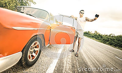 Young hipster fashion man with tattoo taking selfie with vintage car during road trip in Cuba - Travel wanderlust concept Stock Photo