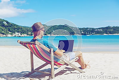 Young hipster man with laptop on tropical beach. Travel, vacation, internet, freelance job concept Stock Photo