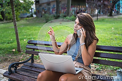 Young hipster millennial freelance woman with cool attitude, expatriate exchange student, sitting in park working online on laptop Stock Photo