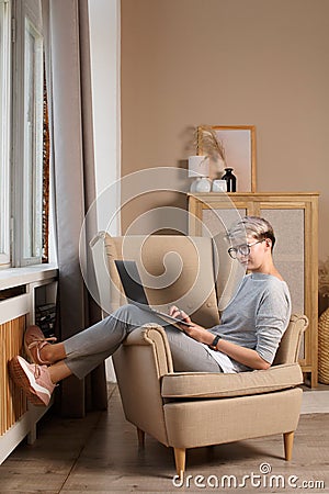 Portrait of pretty smart woman about 30s in casual clothes sitting in a chair typing in laptop Stock Photo