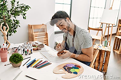 Young hispanic artist man smiling happy painting pottery at art studio Stock Photo