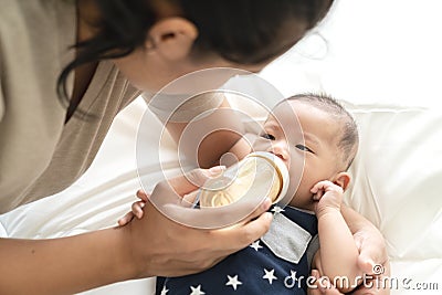 Young hispanic baby or asian infant boy drinking milk from plastic bottle feeding from young parents mother or babysitter Stock Photo