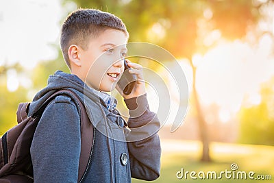 Young Hispanic Boy Walking Outdoors With Backpack Talking on Cell Phone Stock Photo