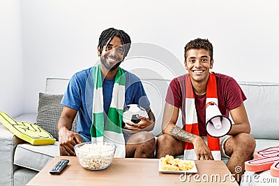 Young hispanic brothers football hooligans holding ball and megaphone looking positive and happy standing and smiling with a Stock Photo