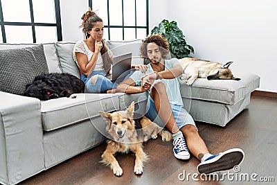 Young hispanic couple with dogs relaxing at home checking the time on wrist watch, relaxed and confident Stock Photo