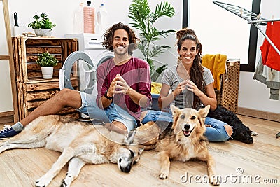 Young hispanic couple doing laundry with dogs hands together and fingers crossed smiling relaxed and cheerful Stock Photo