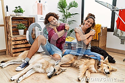 Young hispanic couple doing laundry with dogs hugging oneself happy and positive, smiling confident Stock Photo