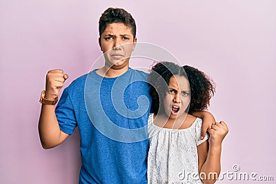 Young hispanic family of brother and sister wearing casual clothes together angry and mad raising fist frustrated and furious Stock Photo