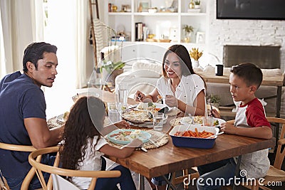 Young Hispanic family sitting at dining table eating dinner together Stock Photo