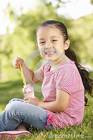 Young Hispanic Girl Blowing Bubbles In Park Stock Photo
