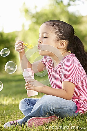 Young Hispanic Girl Blowing Bubbles In Park Stock Photo