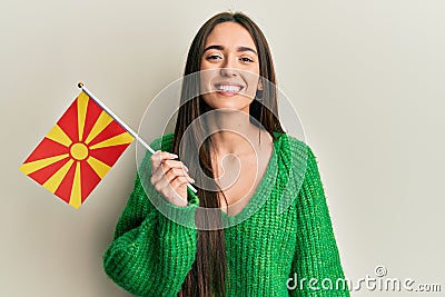 Young hispanic girl holding macedonian flag looking positive and happy standing and smiling with a confident smile showing teeth Stock Photo