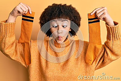 Young hispanic girl holding pair of socks making fish face with mouth and squinting eyes, crazy and comical Stock Photo