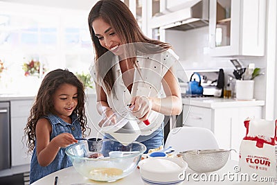 Young Hispanic girl making cake in the kitchen with help from her mum, waist up Stock Photo