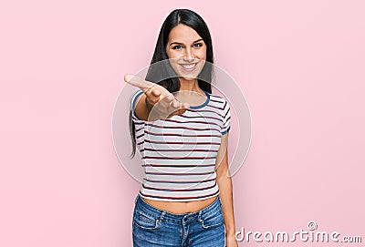 Young hispanic girl wearing casual striped t shirt smiling friendly offering handshake as greeting and welcoming Stock Photo