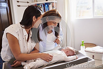 Young Hispanic grandmother and adult daughter playing with her baby son on changing table, waist up Stock Photo