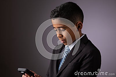 Young Hispanic Little Boy Looking at Phone. Dressed Neatly in a Suit Stock Photo