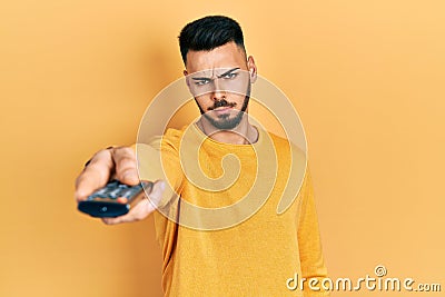 Young hispanic man with beard holding television remote control skeptic and nervous, frowning upset because of problem Stock Photo