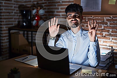 Young hispanic man with beard working at the office at night showing and pointing up with fingers number nine while smiling Stock Photo