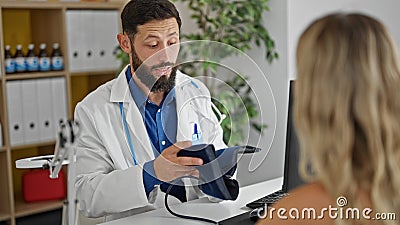 Young hispanic man doctor measuring patient pulse using arm tensiometer at the clinic Stock Photo