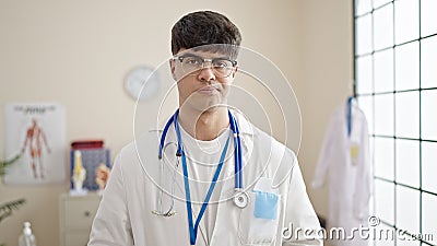 Young hispanic man doctor standing with serious expression at clinic Stock Photo