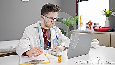 Young hispanic man doctor on video call prescribe pills writing clipboard at clinic Stock Photo