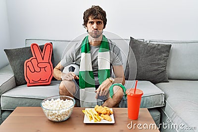 Young hispanic man football hooligan cheering game at home puffing cheeks with funny face Stock Photo