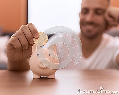 Young hispanic man inserting litecoin crypto currency on piggy bank at home Stock Photo