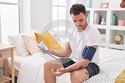 Young hispanic man measuring pulse using tensiometer at bedroom Stock Photo