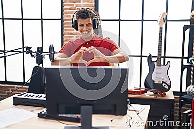 Young hispanic man playing piano keyboard at music studio smiling in love showing heart symbol and shape with hands Stock Photo