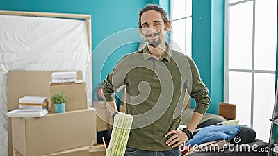 Young hispanic man smiling confident holding paint roller at new home Stock Photo