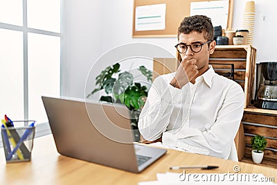 Young hispanic man thinking working with laptop at business office Stock Photo