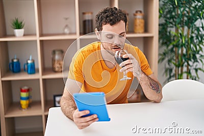 Young hispanic man using touchpad drinkng wine at home Stock Photo