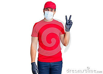 Young hispanic man wearing covid-19 safety mask smiling with happy face winking at the camera doing victory sign Stock Photo