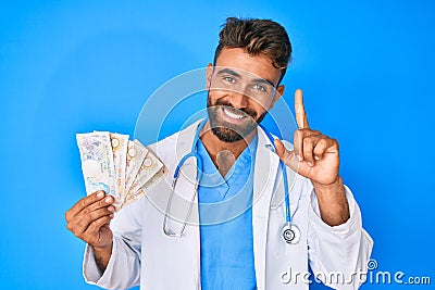 Young hispanic man wearing doctor uniform holding uk pounds banknotes smiling with an idea or question pointing finger with happy Editorial Stock Photo