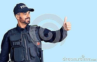 Young hispanic man wearing police uniform looking proud, smiling doing thumbs up gesture to the side Stock Photo