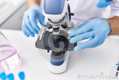 Young hispanic man wearing scientist gloves using microscope at laboratory Stock Photo