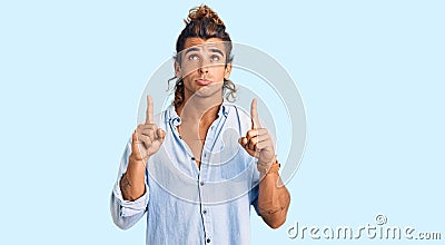 Young hispanic man wearing summer style pointing up looking sad and upset, indicating direction with fingers, unhappy and Stock Photo