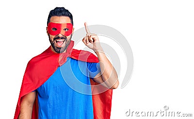Young hispanic man wearing super hero costume pointing finger up with successful idea Stock Photo