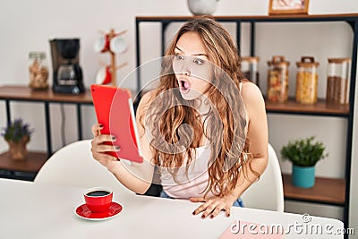 Young hispanic woman doing video call with tablet scared and amazed with open mouth for surprise, disbelief face Stock Photo