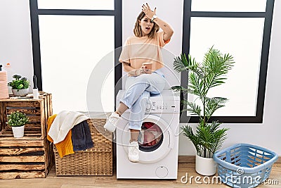 Young hispanic woman drinking coffee waiting for washing machine at laundry room surprised with hand on head for mistake, remember Stock Photo