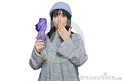 Young hispanic woman holding closed purple umbrella covering mouth with hand, shocked and afraid for mistake Stock Photo