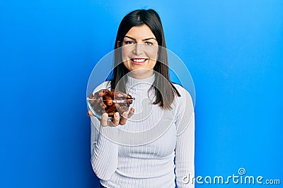 Young hispanic woman holding dates bowl looking positive and happy standing and smiling with a confident smile showing teeth Stock Photo