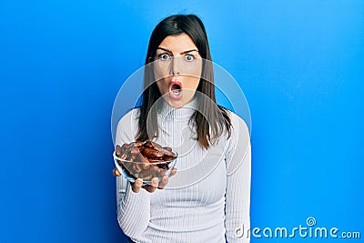 Young hispanic woman holding dates bowl scared and amazed with open mouth for surprise, disbelief face Stock Photo