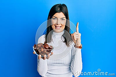 Young hispanic woman holding dates bowl smiling with an idea or question pointing finger with happy face, number one Stock Photo