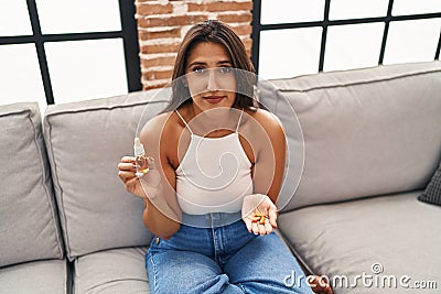 Young hispanic woman holding pills and cbd oil relaxed with serious expression on face Stock Photo