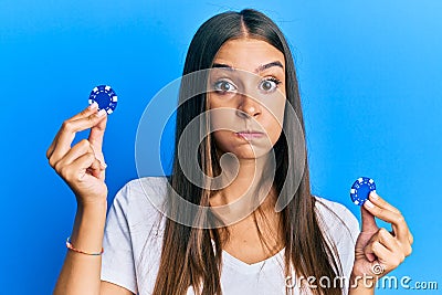 Young hispanic woman holding poker chips puffing cheeks with funny face Stock Photo