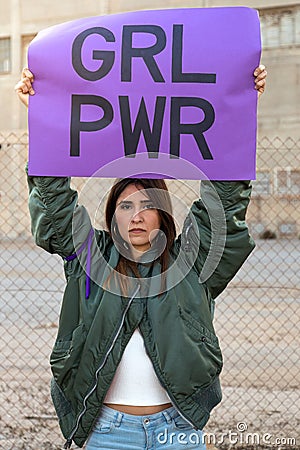 Young hispanic woman looking at camera holding a purple Girl power sign above head in feminist demonstration. Vertical. Stock Photo